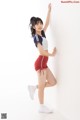 A woman in a white shirt and red shorts leaning against a wall.