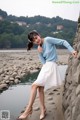 A woman leaning against a stone wall by the water.