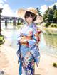 A woman in a blue kimono and a straw hat standing by a river.