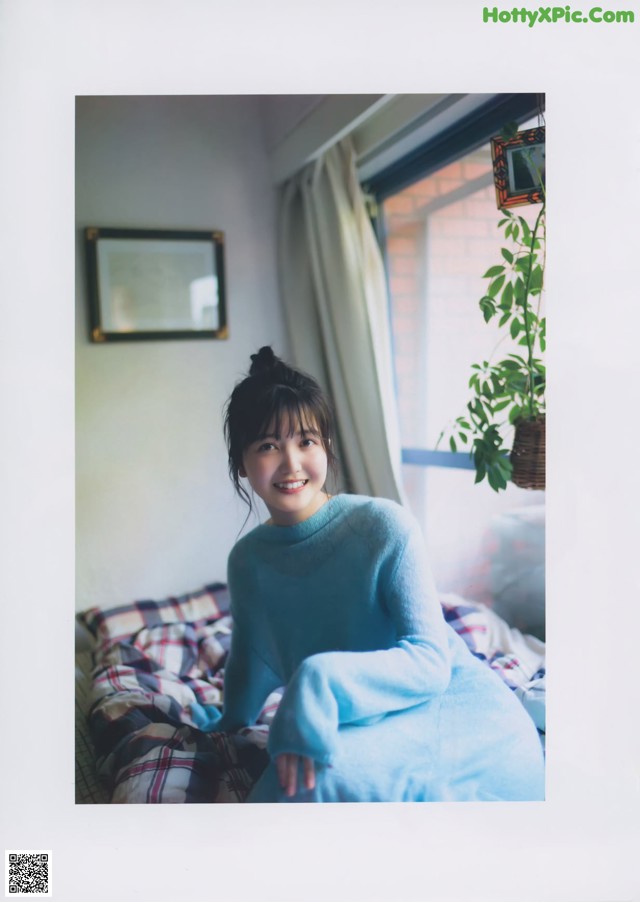 A woman in a blue sweater sitting on a bed.
