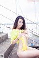 A woman in a yellow bathing suit sitting on a dock.